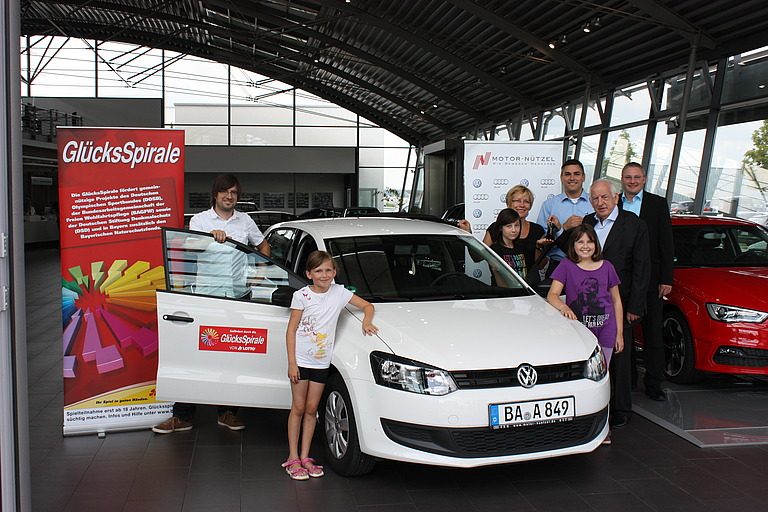 Mehrere Genrationen einer Familie stehen um ein weißes Auto herum.