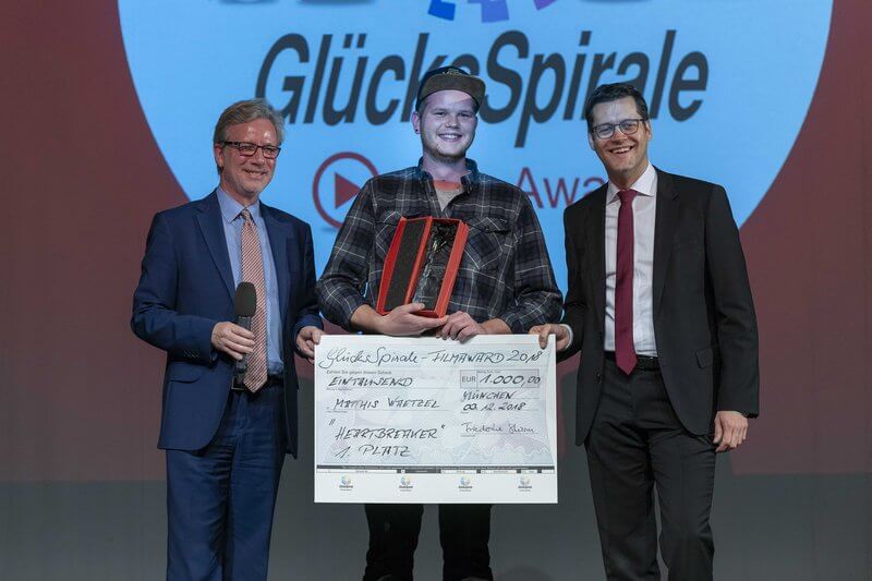 Drei Menschen mit Check, Award und Mikrofon