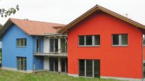 Ein blaues und ein rotes Haus, die durch einen Anbau in der Mitte verbunden sind.
